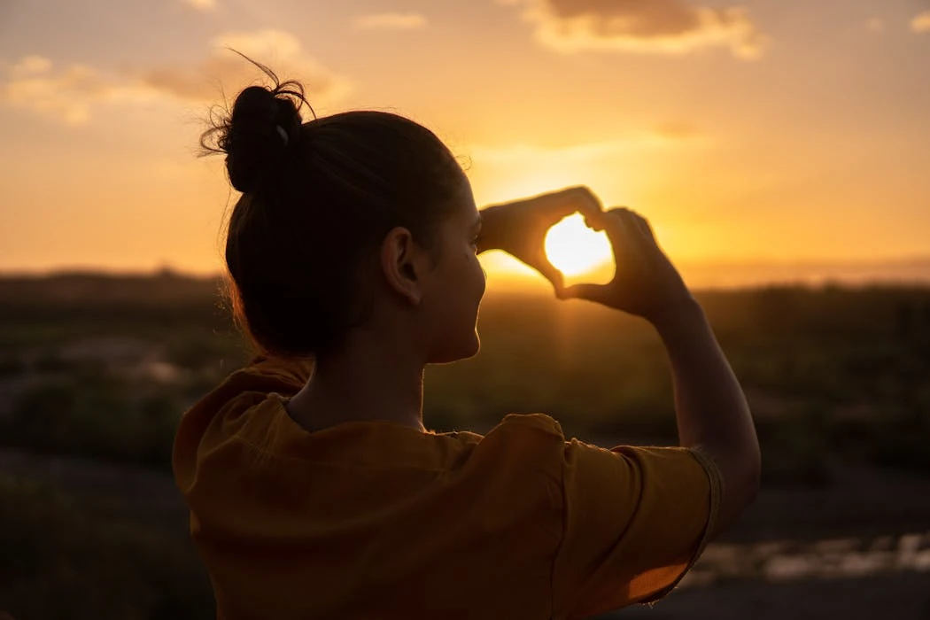 A silhouette of a young woman forming a heart shape at sunset in KelÃ¢at M'Gouna, Morocco.